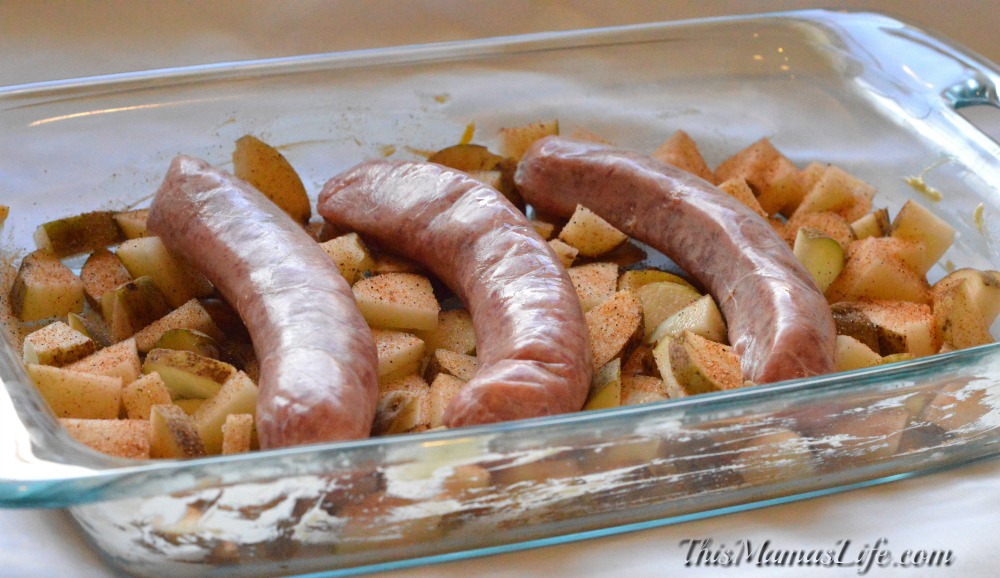 Bratwurst laying on top of potatoes in a baking dish